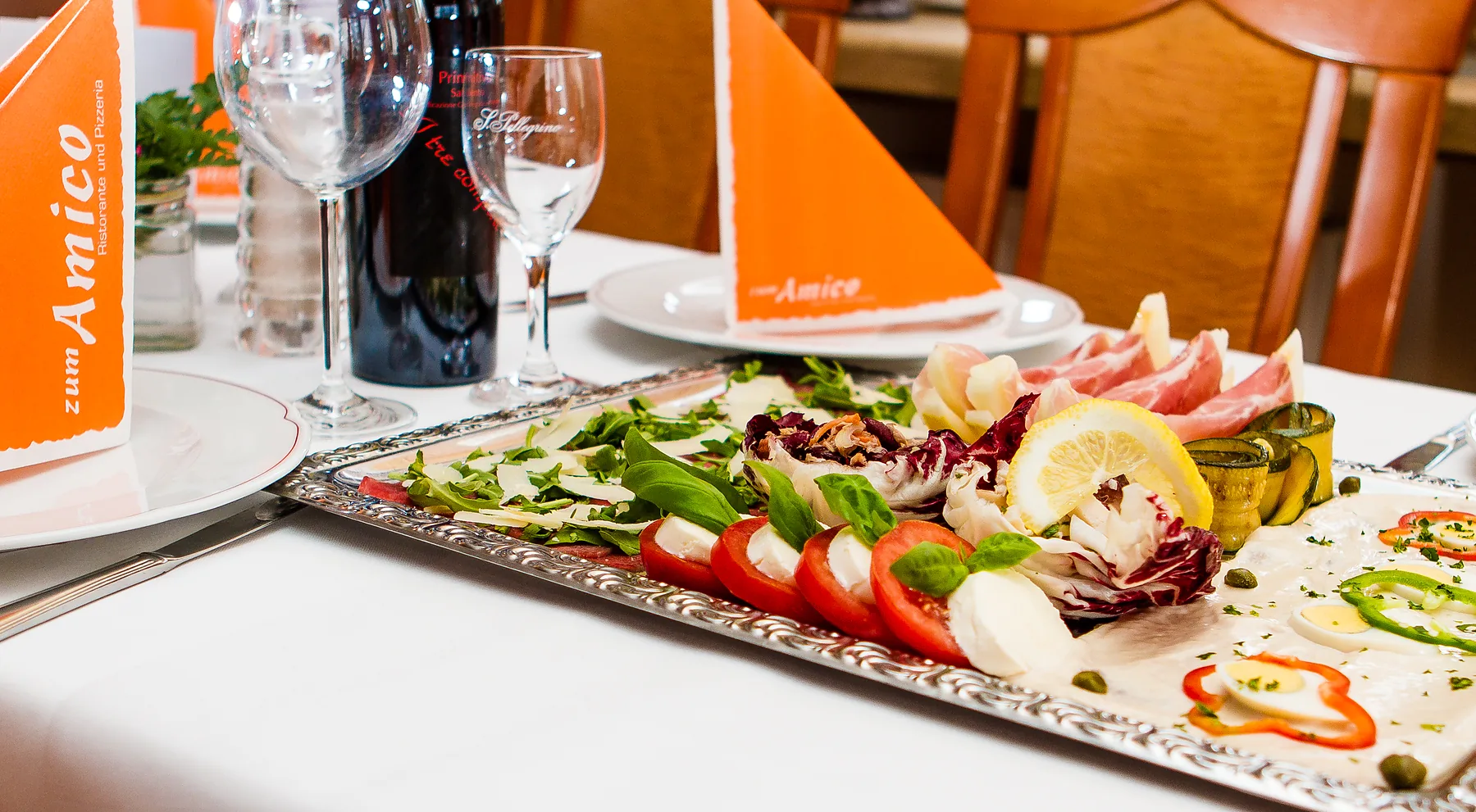 Gedeck mit Weingläsern, Antipasti-Platte und Rotwein